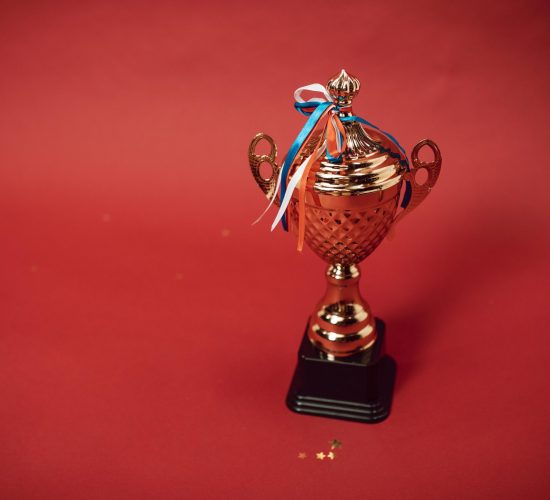 Golden trophy cup with red, blue, and white ribbons on a red backdrop symbolizes achievement and success.