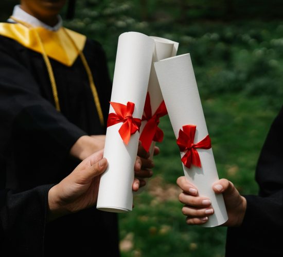 Group of graduates holding diplomas with red ribbons during a ceremony outdoors.